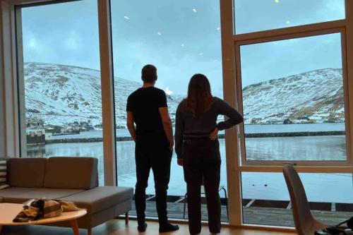 two people standing in a living room looking out of a window at Pauli’s Boathouse in Vestmanna