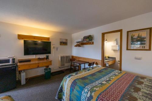 Habitación de hotel con cama, escritorio y TV. en Elk Horn Lodge en Cooke City