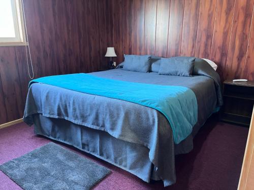 een slaapkamer met een groot blauw bed en houten wanden bij Cabañas Portal del Rio in Nahuentúe