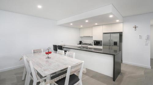 a kitchen with a table with chairs and a refrigerator at Oceans Edge #19 Short Walk To Beach , Shops and Cafes Accom Holidays in Terrigal