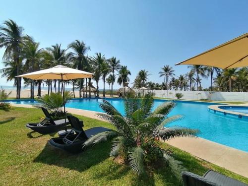 ein Pool mit Stühlen und Sonnenschirmen und einer Palme in der Unterkunft Casa, alberca, club de playa WI-FI en Acapulco in Barra Vieja