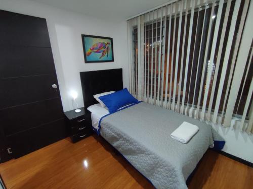 um quarto com uma cama com uma almofada azul e uma janela em Céntrico luminoso y equipado apto em Pasto