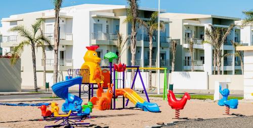 un parque infantil en la arena frente a un edificio en CASA BAY BEACH OMK 2 en Sidi Rahal