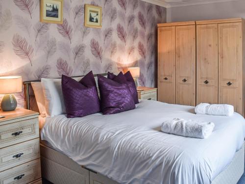 a bedroom with a large bed with purple pillows at Chimney Springs in Ormesby Saint Michael