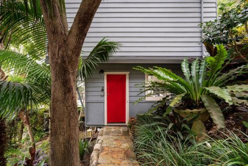 una puerta roja en una casa gris con un árbol en Gull Cottage by Beach Stays, en Church Point
