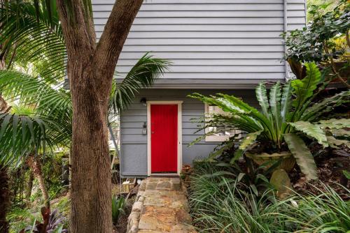 una porta rossa su una casa grigia con un albero di Gull Cottage by Beach Stays a Church Point