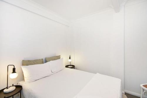a white bedroom with a white bed and two lamps at Parkway Lakehouse in Budgewoi