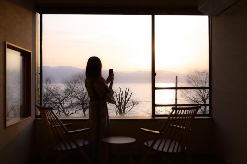 Eine Frau, die aus dem Fenster ein Bild von der Aussicht macht. in der Unterkunft Suwakoen in Suwa
