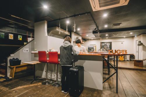 dos personas parados en un mostrador en un restaurante en Tug-B Bar & Hostel, en Otaru