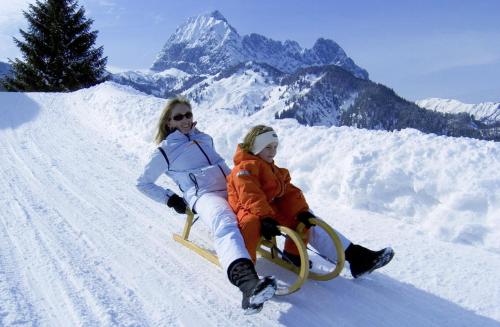 two women are sitting on a sled in the snow at Hotel Gut Kramerhof in Kirchdorf in Tirol