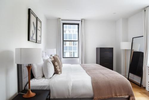 a white bedroom with a bed and a lamp at Midtown East 2br w gym wd nr Grand Central NYC-1146 in New York