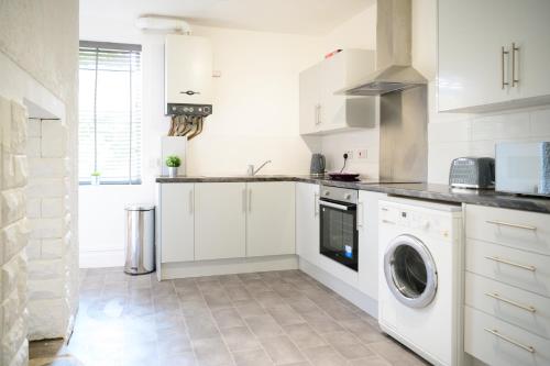 cocina con armarios blancos, lavadora y secadora en Purple Blossom, cosy 2 bed apartment, near Didsbury, free parking, en Mánchester