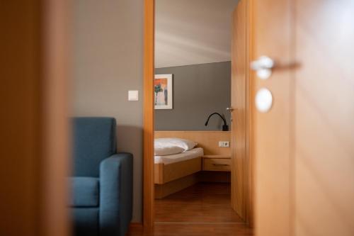 een kamer met een bed, een blauwe stoel en een spiegel bij Sankt Johann Spa Suites & Apartments in Prato allo Stelvio