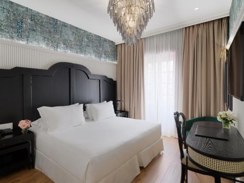 a bedroom with a large bed and a table and a chandelier at H10 Corregidor Boutique Hotel in Seville
