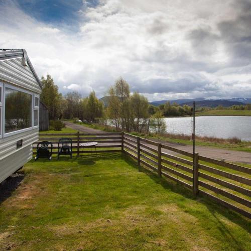 a house with a fence next to a body of water at The Hide near Aviemore in Aviemore