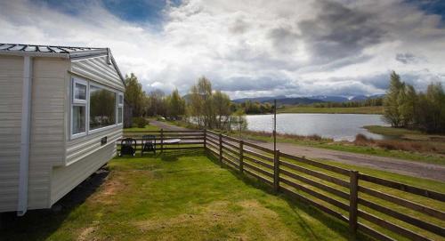 a white house with a fence next to a lake at The Hide near Aviemore in Aviemore