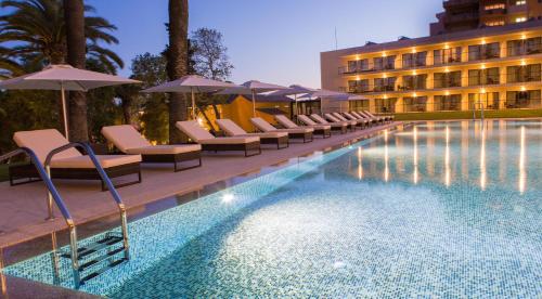 a pool with chairs and umbrellas next to a hotel at Vila Gale Collection Palácio dos Arcos in Oeiras