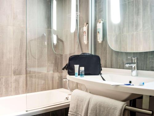 a bathroom with a sink and a shower with a bag on it at Hôtel Ibis Cognac Centre in Cognac