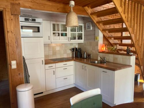 cocina con armarios blancos y techo de madera en Houten chalet/bungalow in het bos, sauna, jacuzzi, en Meijel
