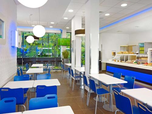 una cafetería con mesas blancas y sillas azules en ibis budget Wiesbaden Nordenstadt, en Wiesbaden