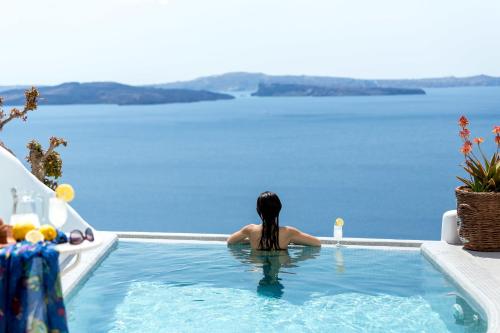 a woman sitting in a swimming pool looking out at the water at Filotera Suites in Oia