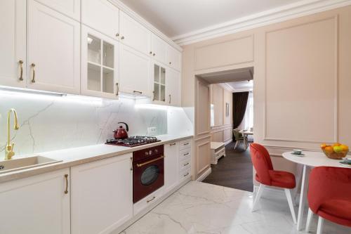 a kitchen with white cabinets and a table and red chairs at Apartment near the Opera Theater in Lviv