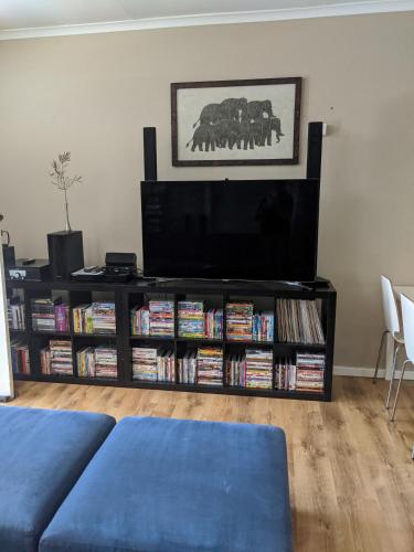 a living room with a television and a book shelf filled with dvds at Blueshack - Walking Distance To Foreshore in Guilderton