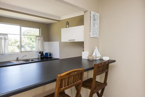 a kitchen with a black counter and two wooden chairs at Blueshack - Walking Distance To Foreshore in Guilderton