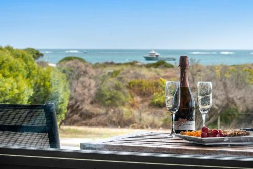 a table with a bottle of wine and wine glasses at Sunset View- Ocean Views in Lancelin