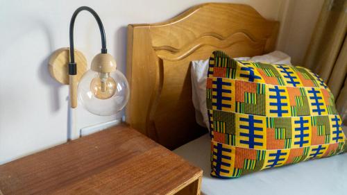 a bed with a lamp and a bag on a table at Sign of Silence Hostel in Kumasi