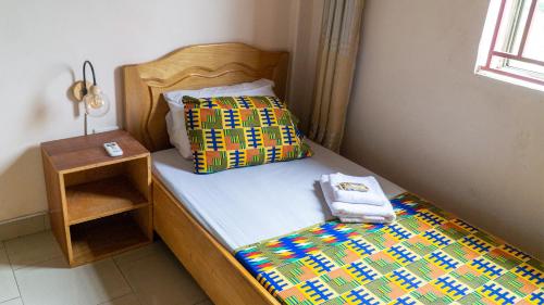 a bed with a colorful comforter and a night stand at Sign of Silence Hostel in Kumasi