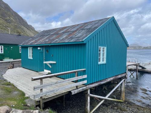 a blue building on a dock next to the water at Kræmmervika Rorbuer - Rustic Cabins in Lofoten in Ballstad
