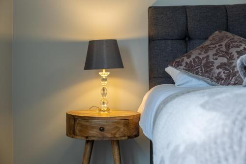 a lamp on a wooden table next to a bed at Wonderful Townhouse with BBQ Backyard in Great Yarmouth