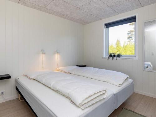 a white bedroom with a large bed with a window at Holiday home Læsø II in Læsø