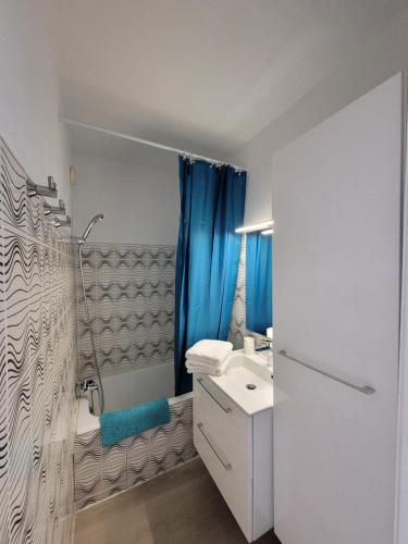 La salle de bains est pourvue d'un lavabo et d'une douche avec des rideaux bleus. dans l'établissement Blue Sea Vue mer - Village naturiste Héliopolis, au Cap d'Agde
