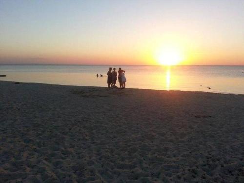 Mellita的住宿－Coeur des iles，日落时分在海滩上散步的三人