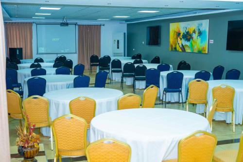 a conference room with white tables and chairs and a screen at Midindi Hotel in Accra