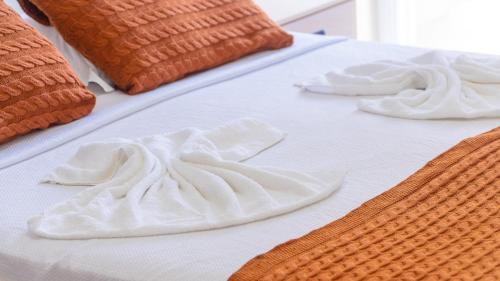 two white towels on a bed with orange pillows at Residencial Las Salinas in Maresias