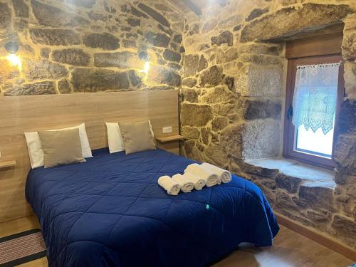 a bedroom with a blue bed in a stone wall at Casinhas da Capela in Tourém