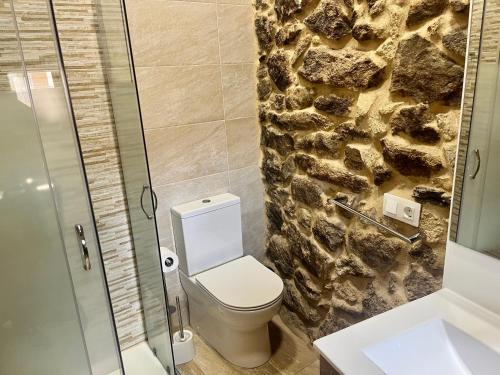 a bathroom with a toilet and a stone wall at Casinhas da Capela in Tourém