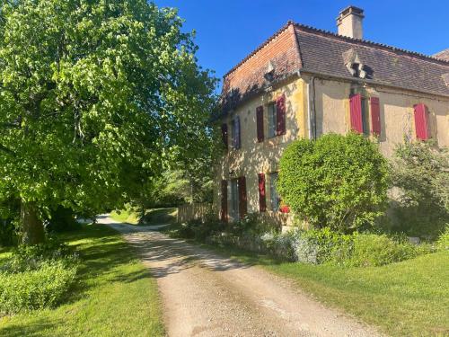 una casa vieja con persianas rojas en un camino de tierra en La chambre du tilleul en Capdrot