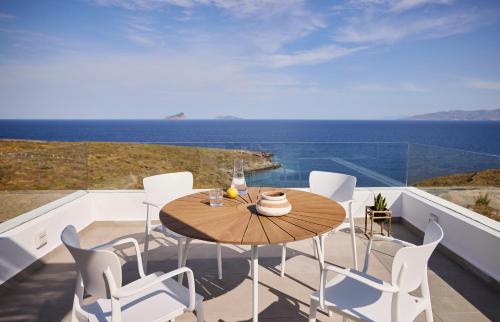 uma varanda com uma mesa de madeira e cadeiras brancas em Ianemi Suites by K4 Kythnos em Kythnos