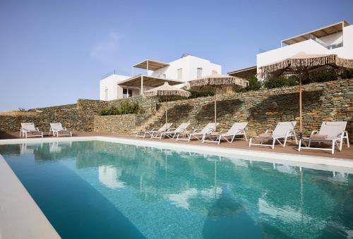 a swimming pool with chairs and a house in the background at Ianemi Suites by K4 Kythnos in Kithnos