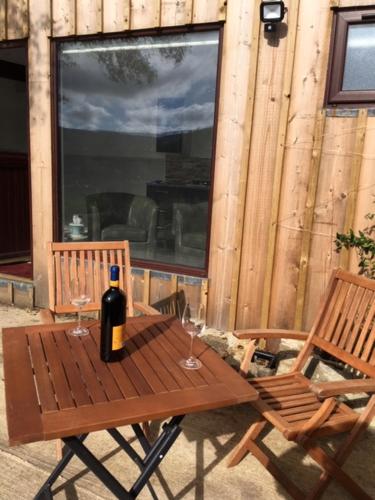 a wooden table with a bottle of wine and two chairs at Ade's River Cabin in Lettermacaward