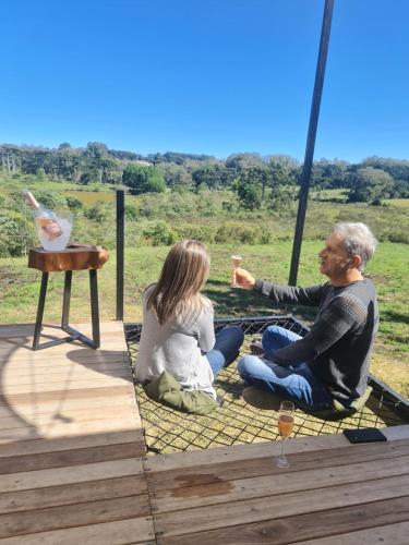 a man and woman sitting on a blanket with a glass of wine at Casa Container - Haupt Village in Farroupilha