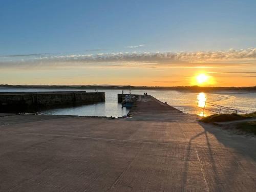 a pier with the sun setting over the water at Rockview Beadnell - Perfect Family Retreat in Beadnell