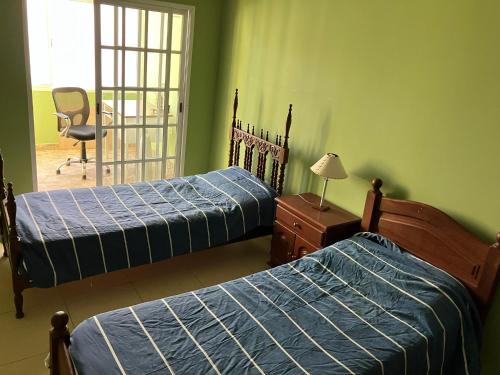 2 camas en una habitación con paredes verdes y una silla en Maximo confort en Salta en Salta