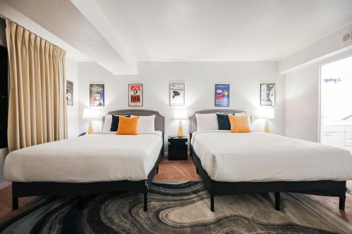 2 camas en una habitación con paredes blancas y almohadas de color naranja en StripViewSuites at Jockey Club, en Las Vegas