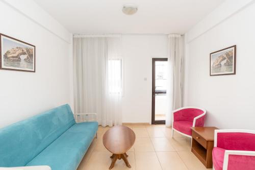 a living room with a blue couch and pink chairs at Flora Hotel Apartments in Protaras