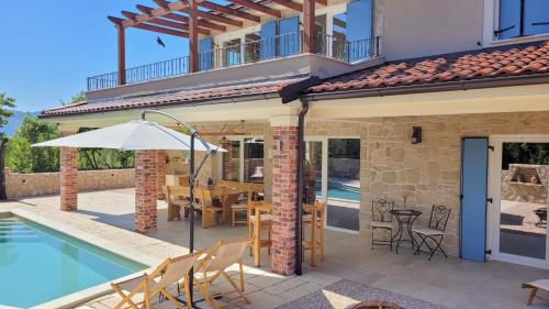 ein Haus mit einem Pool mit einem Tisch und einem Sonnenschirm in der Unterkunft Villa Alara - charming villa with heated swimming pool in Milohnići